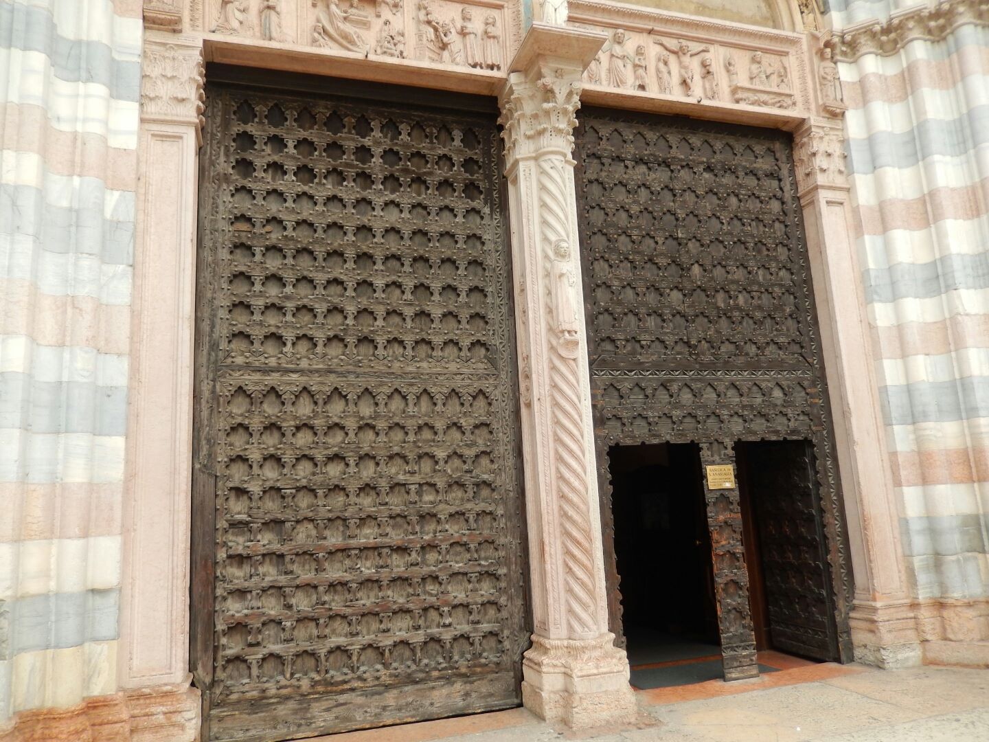The 15th century portal has two doors, and is enclosed into a Gothic structure (1330) with arches supported by ornamental columns in red, black and white marble.
